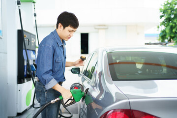 Happy cheerful Asian middle adult man refueling his car at self-service gas station.