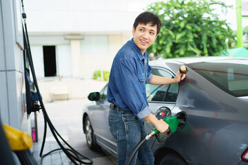 Happy cheerful Asian middle adult man refueling his car at self-service gas station.
