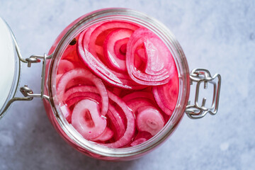 Close up pickled red onions rings in glass jar on a gray background. Fermented vegetarian food...