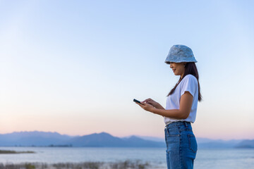 Traveler asian woman using mobile phone travel in lake at sunset in Phetchaburi Thailand