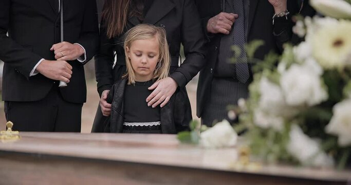 Death, grief and girl at funeral with flower on coffin, family and sad child at service in graveyard for respect. Roses, loss and people at wood casket in cemetery with kid crying at grave for burial