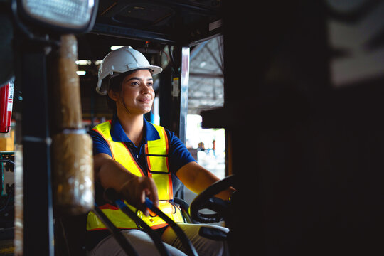 Female worker driving a forklift and looking for something in a warehouse. Workers work in the warehouse.