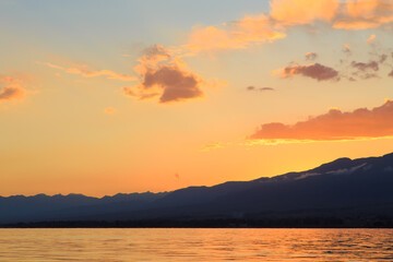 Fototapeta premium Beautiful cloudy sunset over the sea and mountains. Bright sky in the rays of the orange sun. natural texture