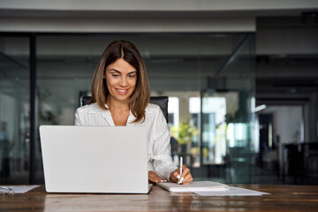 Middle-age Hispanic woman using laptop computer for business studying, watch online virtual webinar training meeting,video call. Focused mature 40s years Latin businesswoman work in office, copy space