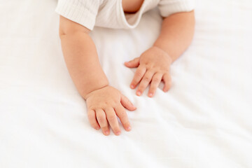 hands of a small baby on a white cotton bed at home, small fingers of a child close-up