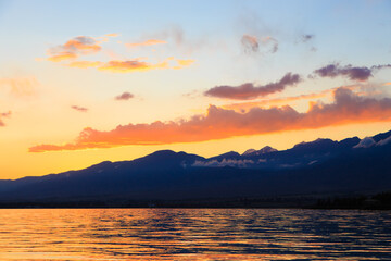 Colorful sunset on the sea. Mountain lake in the rays of the orange sun. Kyrgyzstan, Lake Issyk-Kul.