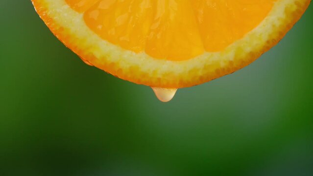 Drops of juice or water close-up drop from slice of ripe orange. Concept of fresh vegetables and fruits. Orange with dripping clear juice on green background. Slow motion