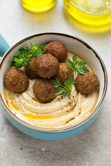 Turquoise serving bowl with hummus and falafel, vertical shot on a beige stone background, middle closeup