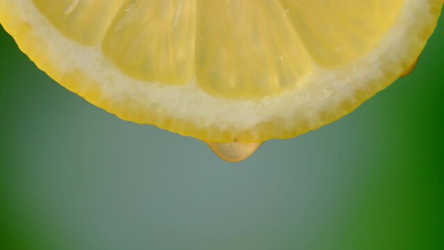Drops of juice or water close-up from slice of ripe lemon. Concept of fresh vegetables and fruits. lemon with macro dripping clear juice on green background. Slow motion