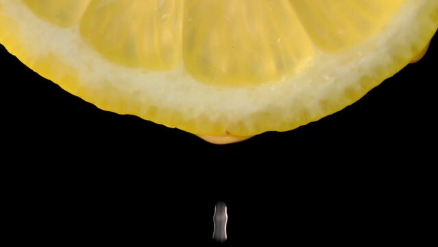 Drops of juice or water close-up from slice of ripe lemon. Concept of fresh vegetables and fruits. lemon with macro dripping clear juice on black background. Slow motion