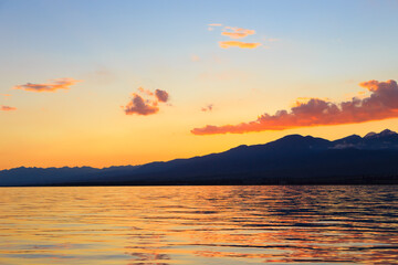Fototapeta premium Beautiful cloudy sunset over the sea and mountains. Bright sky in the rays of the orange sun. natural texture