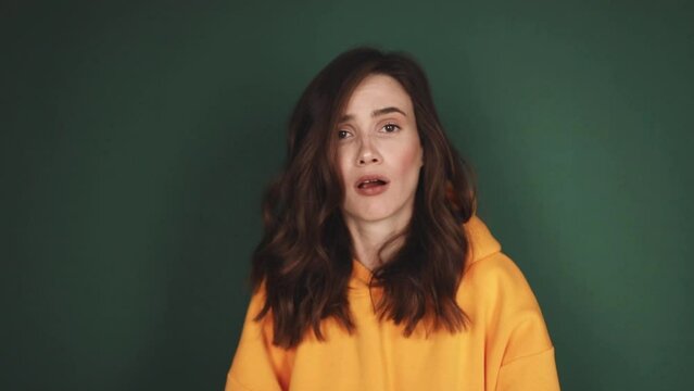 You lose! Brunette young woman wear yellow hoody making loser gesture, L sign on forehead, teasing and accusing for defeat, expressing disrespect. Indoor studio shot isolated on green background.