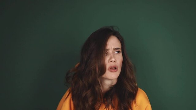 Skeptical beautiful caucasian female wear yellow hoody standing on green background looking by side, listen and wave head no with disappointment. Confused woman. 
