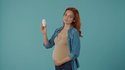 Portrait of a pregnant woman with a jar of vitamin in the studio on a blue background. Health care and prenatal vitamans on pregnancy time. Illness and medicine while pregnancy.