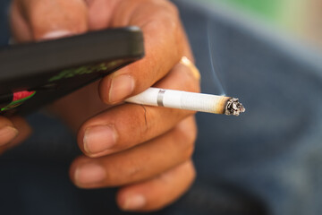 A young man holding a cigarette in his left hand. Right hand holdding smartphone