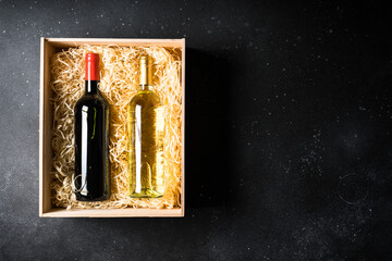 Red and white wine at black background. Two bottles in wooden box. Top view with copy space.