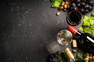 Red and white wine at black background. Glasses of wine, bottles and fresh crape. Top view with copy space.