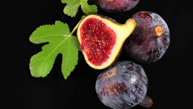 Fig fruits. Ripe sweet fresh figs fruit with leaves close up, rotating on black background , top view. Macro shot of healthy organic figs 