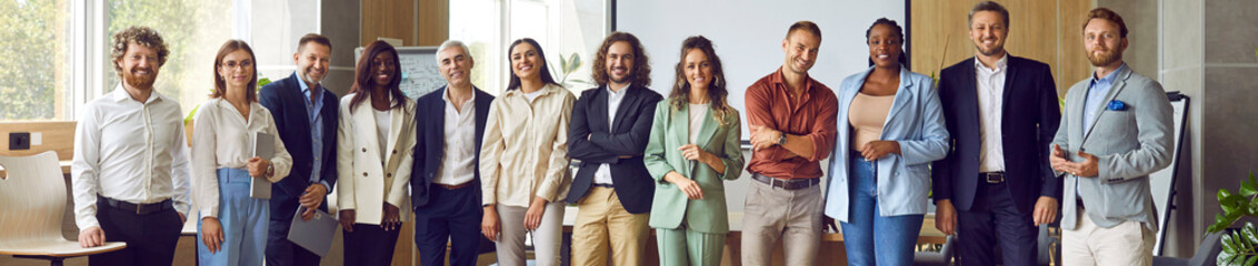 Group of business multiethnic people men and women looking cheerful at camera and smiling indoors. Company employees or group of staff standing in office confidently. Team work concept. Banner.