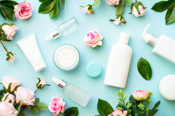 Natural cosmetic products on blue background. Cream, serum, tonic with green leaves and flowers. Skin care concept.