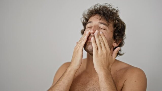 Young hispanic man applying skin face lotion shirtless over isolated white background