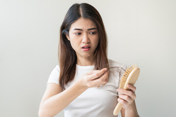 Serious asian young woman holding brush holding comb, hairbrush with fall black hair from scalp after brushing, looking on hand worry about balding. Health care, beauty treatment, hair loss problem.