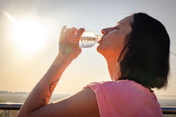 Lady with tattoo on arm drinks water from plastic bottle. Respite between exercise and enjoying warm summer day closeup