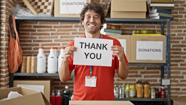 Young hispanic man volunteer smiling confident holding thank you banner at charity center