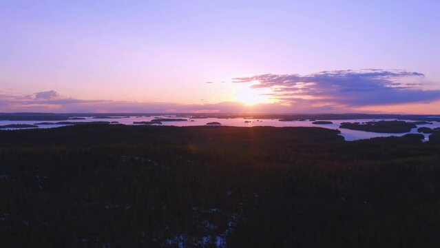 Beautiful purple sunset drone footage horizontal pan over the forest with a frozen lake in the horizon (Konnevesi National Park, Finland)
