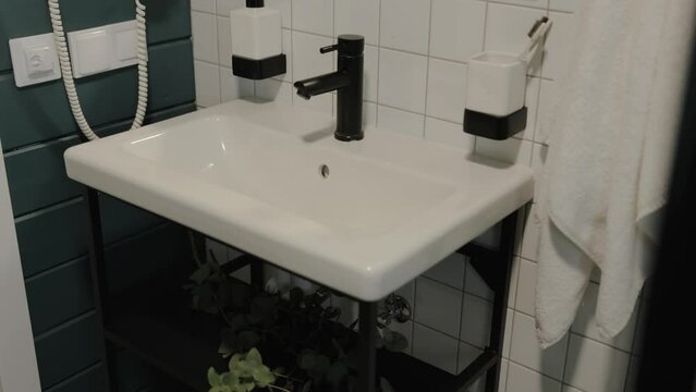 Dolly shot of modern minimal clean bathroom with white sink and black tap, a white towel hangs on the wall, minimalist interior slow motion.
