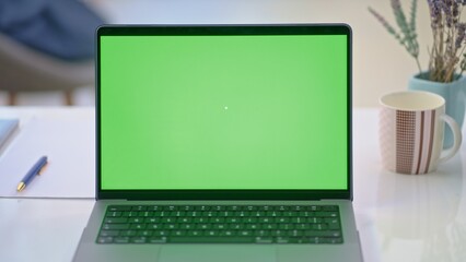 Laptop computer on desk with blank green screen