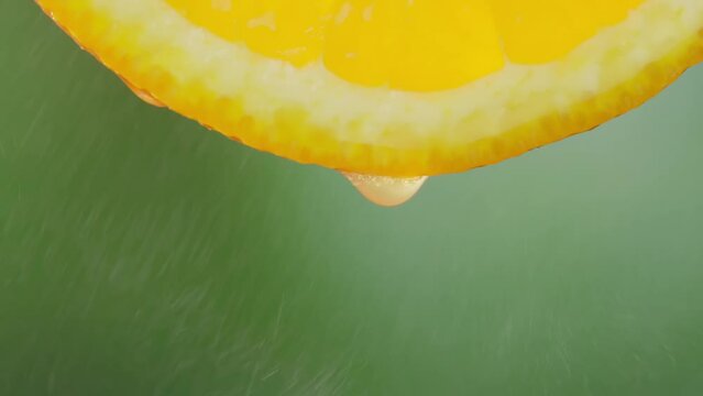 Drops of juice or water close-up drop from slice of ripe orange. Concept of fresh vegetables and fruits. Orange with dripping clear juice on green background. retarded motion