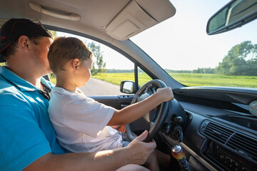 Father and son happily spend time together. A father teaches a small child to drive a car on a forest road. The boy is happy that his father allowed him to drive the car.