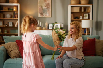 Daughter congratulating her mother and giving her bouquet of flowers at home