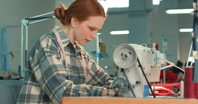 Smiling successful woman seamstress sews fashion clothes use sewing machine at workplace. Beautiful female dressmaker skilled clothing designer create handmade garment at workshop, looking at camera