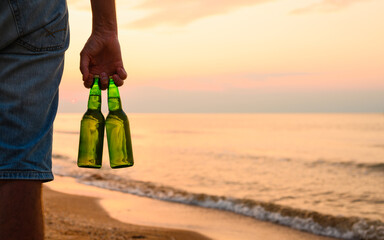 Two bottles of beer in a man's hand. Sunset on the sea with a friendly company. close-up