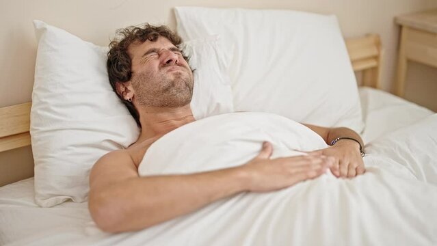 Young hispanic man suffering for stomach ache lying on bed shirtless at bedroom