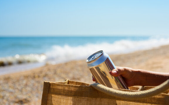 A girl on the beach takes out a can of cold drink from her bag. Summer vacation by the sea