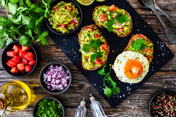 Tasty bruschetta with sunny side up egg, guacamole, tomato, and onion on wooden table
