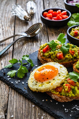 Tasty bruschetta with sunny side up egg, guacamole, tomato, and onion on wooden table
