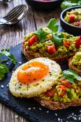 Tasty bruschetta with sunny side up egg, guacamole, tomato, and onion on wooden table
