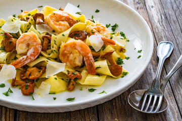 Tagliatelle with chanterelle mushrooms, seared prawns and   Parmigiano Reggiano on wooden table
