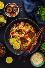 Asian food - roast beef, noodles and stir fried vegetables on wooden table
