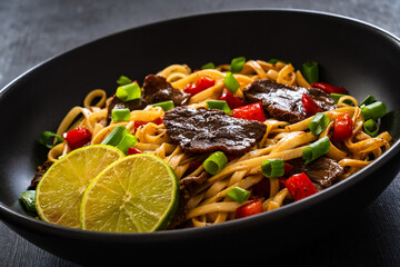 Asian food - roast beef, noodles and stir fried vegetables on wooden table
