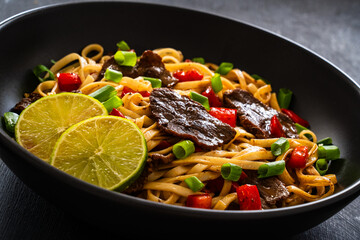 Asian food - roast beef, noodles and stir fried vegetables on wooden table
