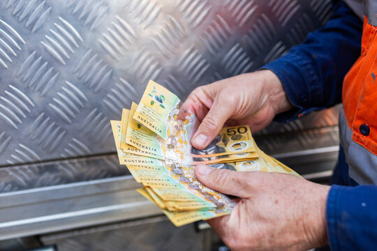 Hands of a handyman counting cash beside tradie ute