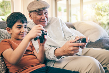 Family, fun and a boy gaming with his grandfather on a sofa in the living room of their home during...