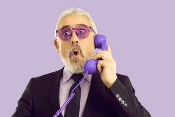 OMG really. Head shot of handsome bearded senior business man holding phone receiver and looking...