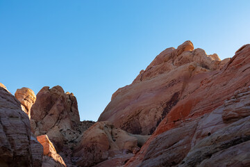 Fototapeta na wymiar Scenic view on wall of striated red and white rock formations along the White Domes Hiking Trail in Valley of Fire State Park in Mojave desert, Nevada, USA. First sunlight touches arid landscape