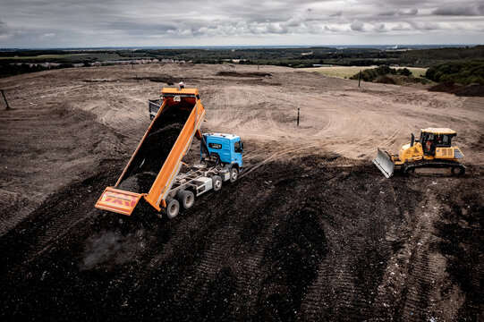 Aerial view of a tipper truck with raised trailer unloading landfill waste 